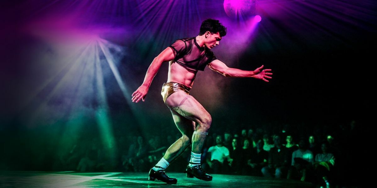 Wake Production Image - Male Dancer in gold hotpants and mesh top tap dancing.