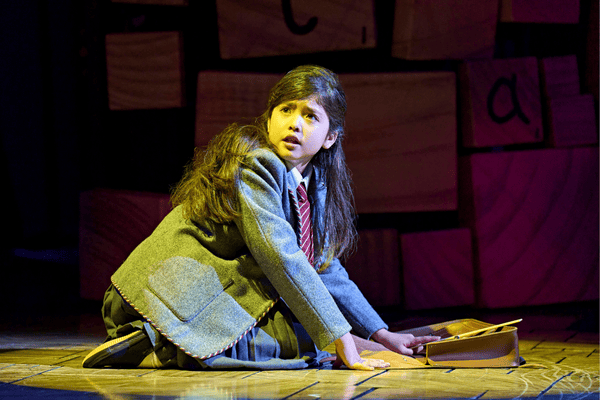 A scene from Matila The Musical featuring girl in grey school uniform kneeling down.