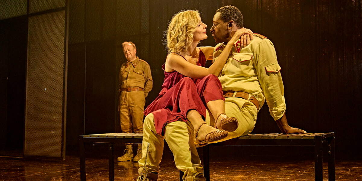 Caitlin Fitzgerald as Desdemona sits on David Harewood's (Othello's) lap while Toby Jones as Iago watches on from the corner