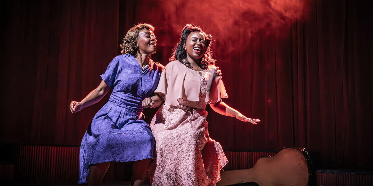 Two women perform on stage in Marie and Rosetta, singing together under warm red lighting, capturing the show’s powerful musical partnership.