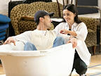 Two people share a lighthearted moment while sitting in a vintage bathtub. They appear to be enjoying each other's company in a casual indoor setting.