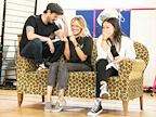 Three people are sitting on a vintage couch, laughing and sharing a light moment. The setting appears casual and playful.