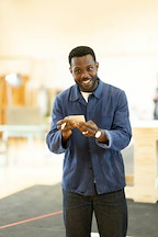 A person is smiling while holding a small card. They are in a well-lit indoor space with wooden structures.