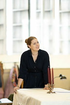 A person stands near a table, smiling and engaged in conversation. Candles are placed in a decorative holder on the table.