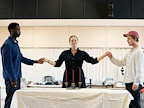 Three people hold hands around a table with candles. They appear engaged in a meaningful moment.