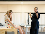 Two individuals share a light-hearted moment in a studio setting. One person laughs while sitting, and the other gestures animatedly.