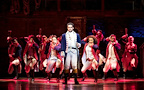 A group performs on stage, showcasing dynamic choreography. The central figure holds a staff confidently.