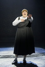 A performer sings on stage, wearing a black dress with a white collar. The spotlight highlights the captivating scene.
