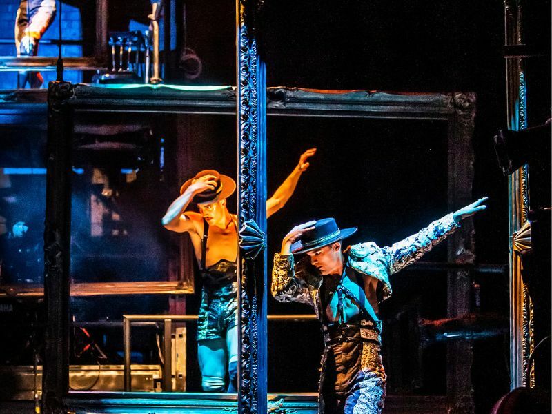 Image: cast members holding their hats and holding their arms out.