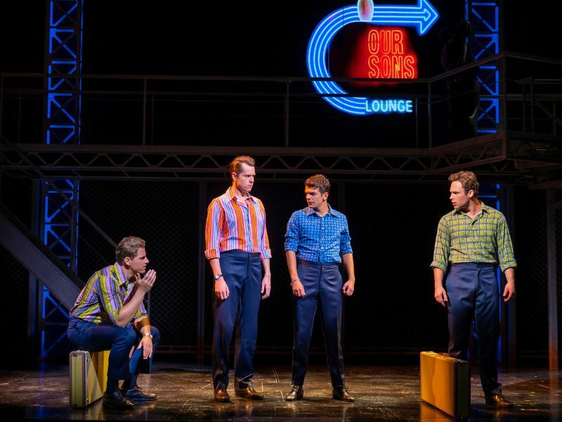 Image: the cast of Jersey Boys on stage. Wearing different coloured shirts. They are stood in different positions and are looking in different directions. 