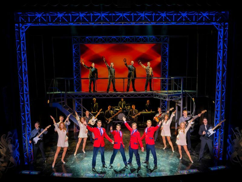 Image: the four main cast of Jersey Boys on stage, holding their arms out. They are wearing red blazers.