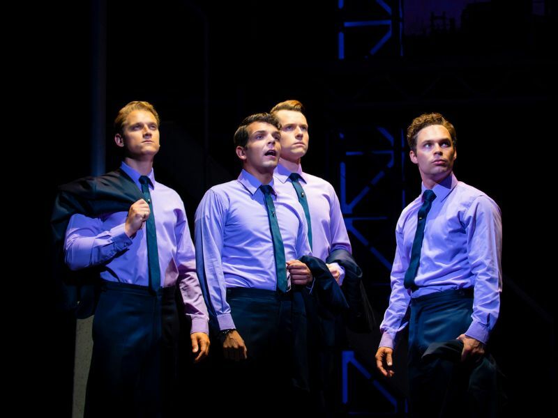 Image: the four main cast of Jersey Boys looking off into the distance. They are wearing blue shirts and ties.