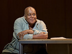 A person sits at a table, smiling and engaging in conversation. The setting has a warm, intimate atmosphere.