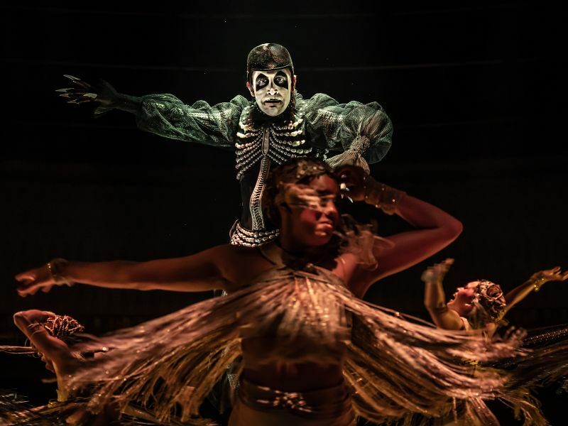 Callum Scott Howells as Emcee Cabaret. He is dressed in a green, skeleton like costume and is looking intently into the camera. 