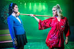 Two individuals face off on stage, with one holding a mallet. The atmosphere is dramatic with green lighting.