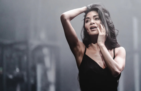 Nicole Scherzinger as Norma Desmond in Sunset Boulevard, wearing a black dress with smoke in the background.